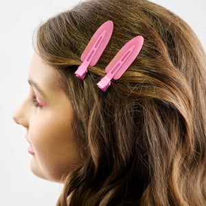 Girl with long brown hair wearing two pink hair clips on a white background