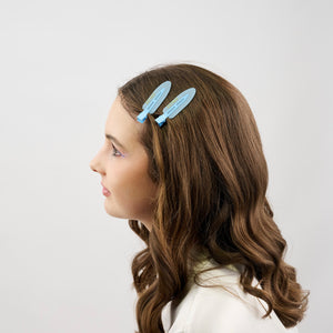 Girl with long brown hair wearing two blue hair clips on a white background