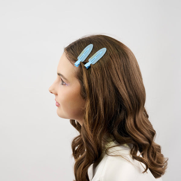 Girl with long brown hair wearing two blue hair clips on a white background
