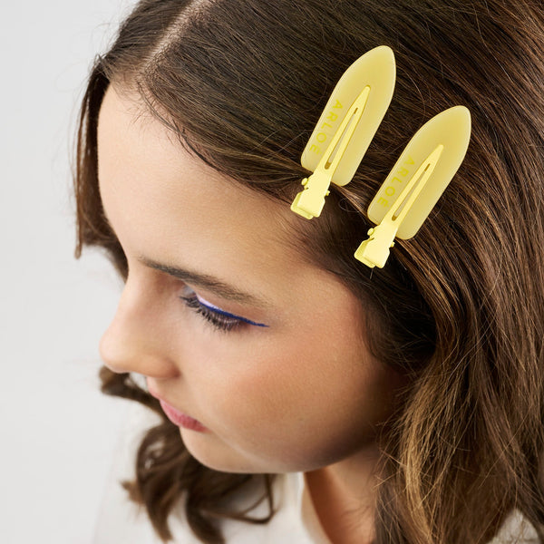 Girl with long brown hair wearing two yellow hair clips on a white background