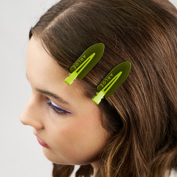 Girl with long brown hair wearing two green hair clips on a white background
