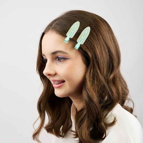 Woman with wavy hair wearing two mint coloured hair clips on a plain background
