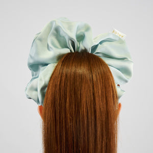 Person wearing a light blue satin hair scrunchie on a plain background