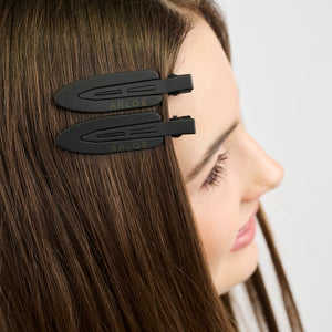 Girl with long brown hair wearing two black hair clips on a white background