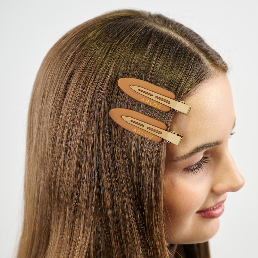 Two peach-colored hair clips with gold accents on a white background, branded 'ARLOE'.